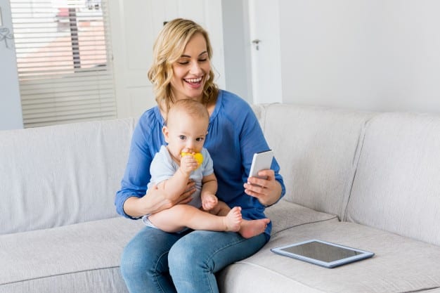 mother holding baby boy and using smartphone